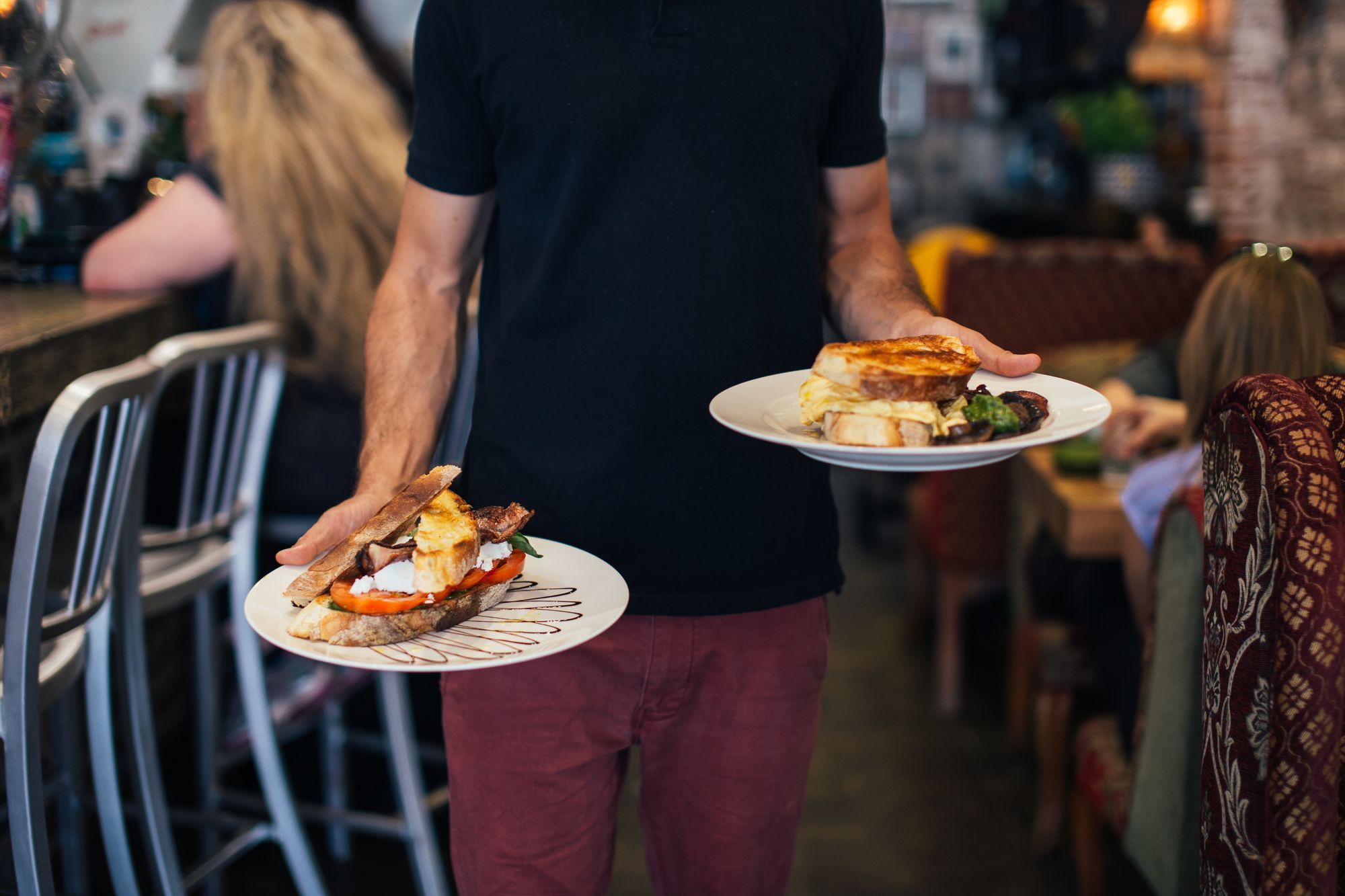 A waiter carrying two plated meals across a busy restaurant floor